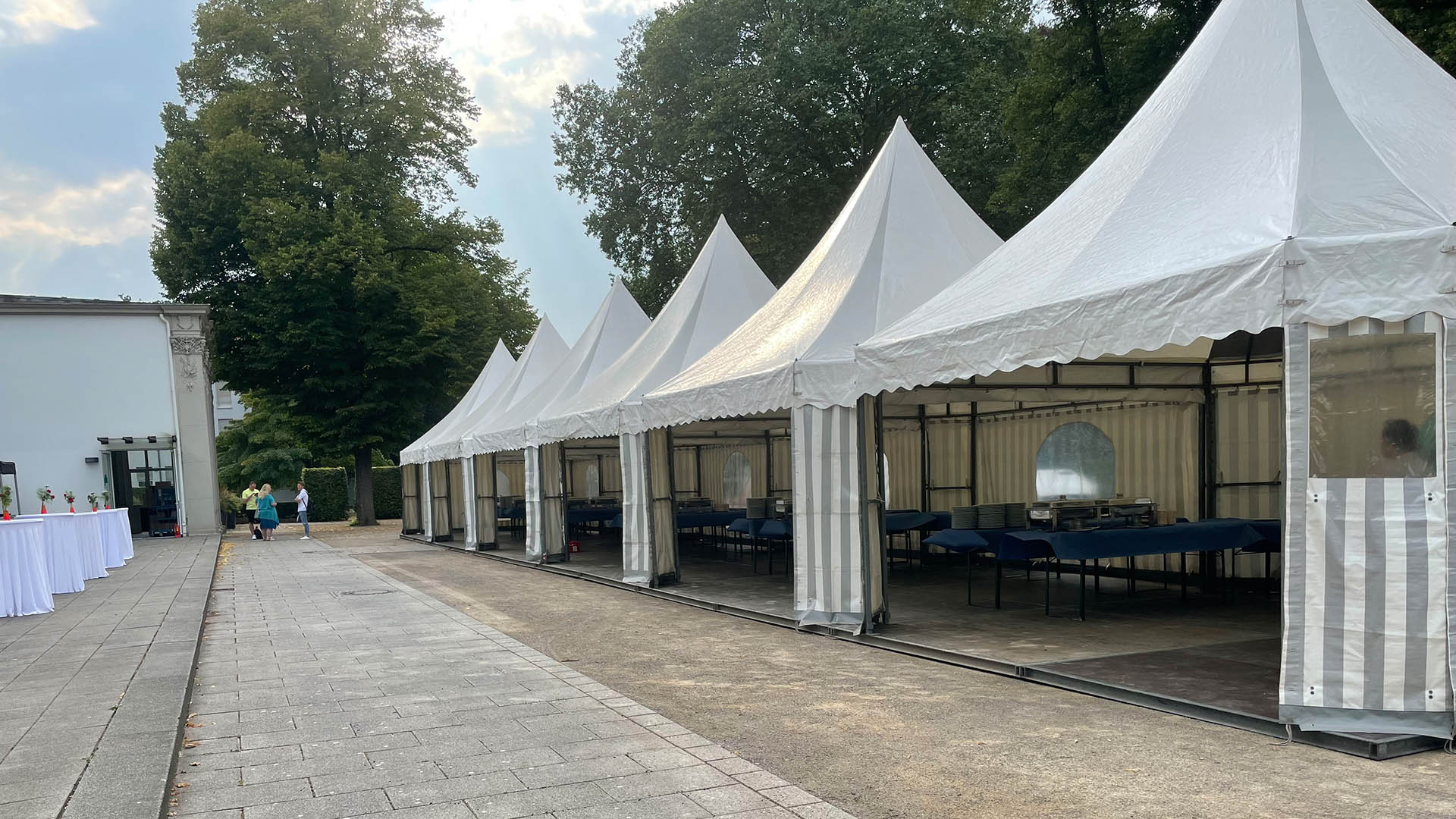 Reihen von weißen Pavillons in einem Park mit leeren Bänken und Bäumen im Hintergrund