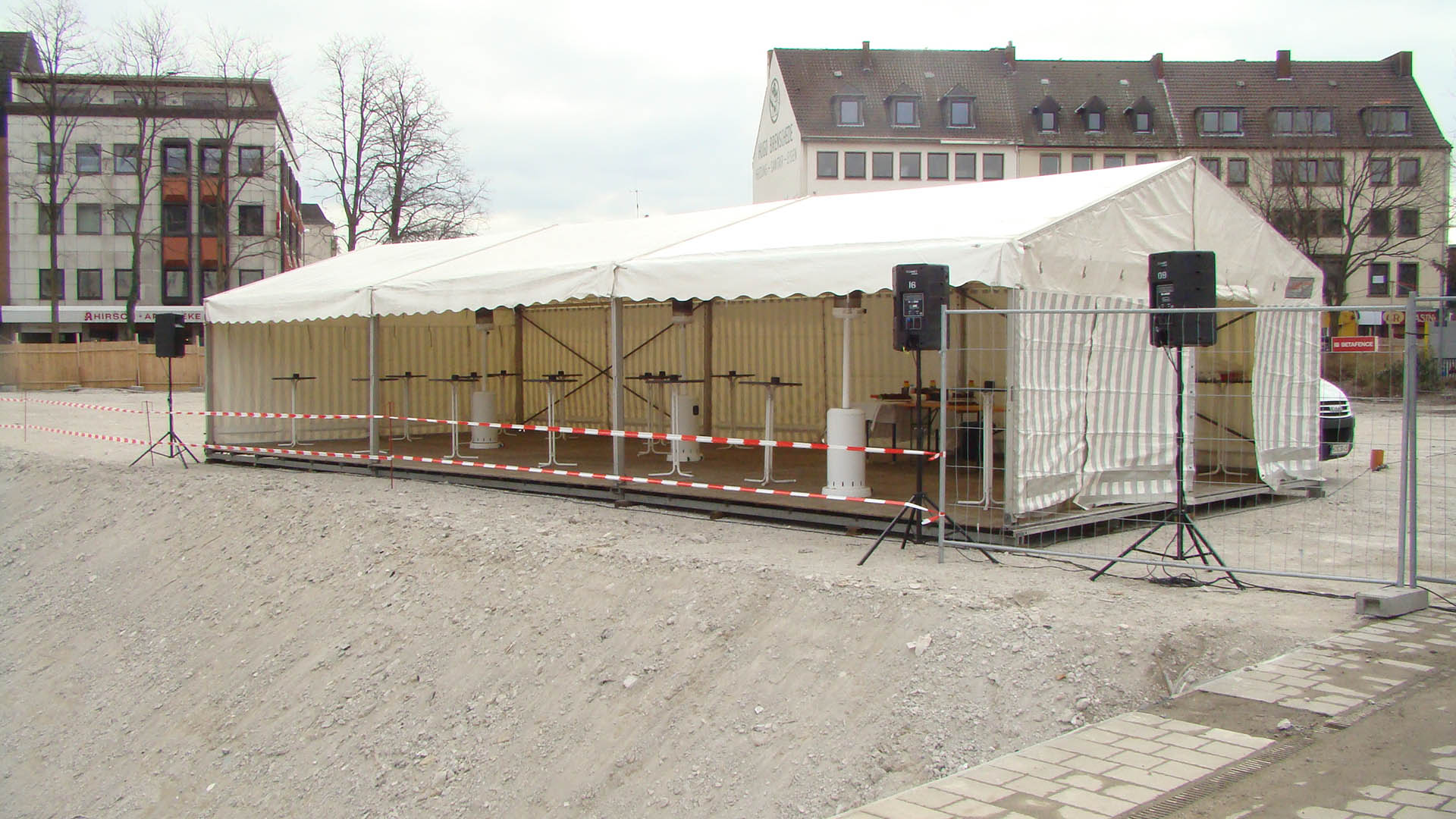 Eine weiße Festzeltkonstruktion steht auf einer Baustelle, innen mehrere Stehtische