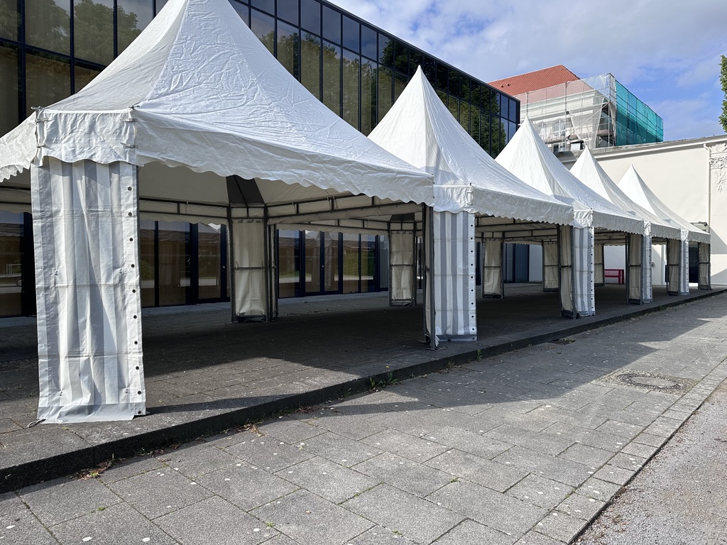 Mehrere weiße Pavillons stehen leer nebeneinander vor einem modernen Gebäude