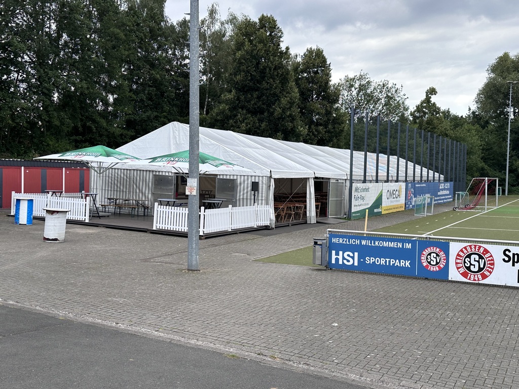 Großes weißes Festzelt mit Pavillons und Holzmöbeln beim Fußballplatz im Grünen