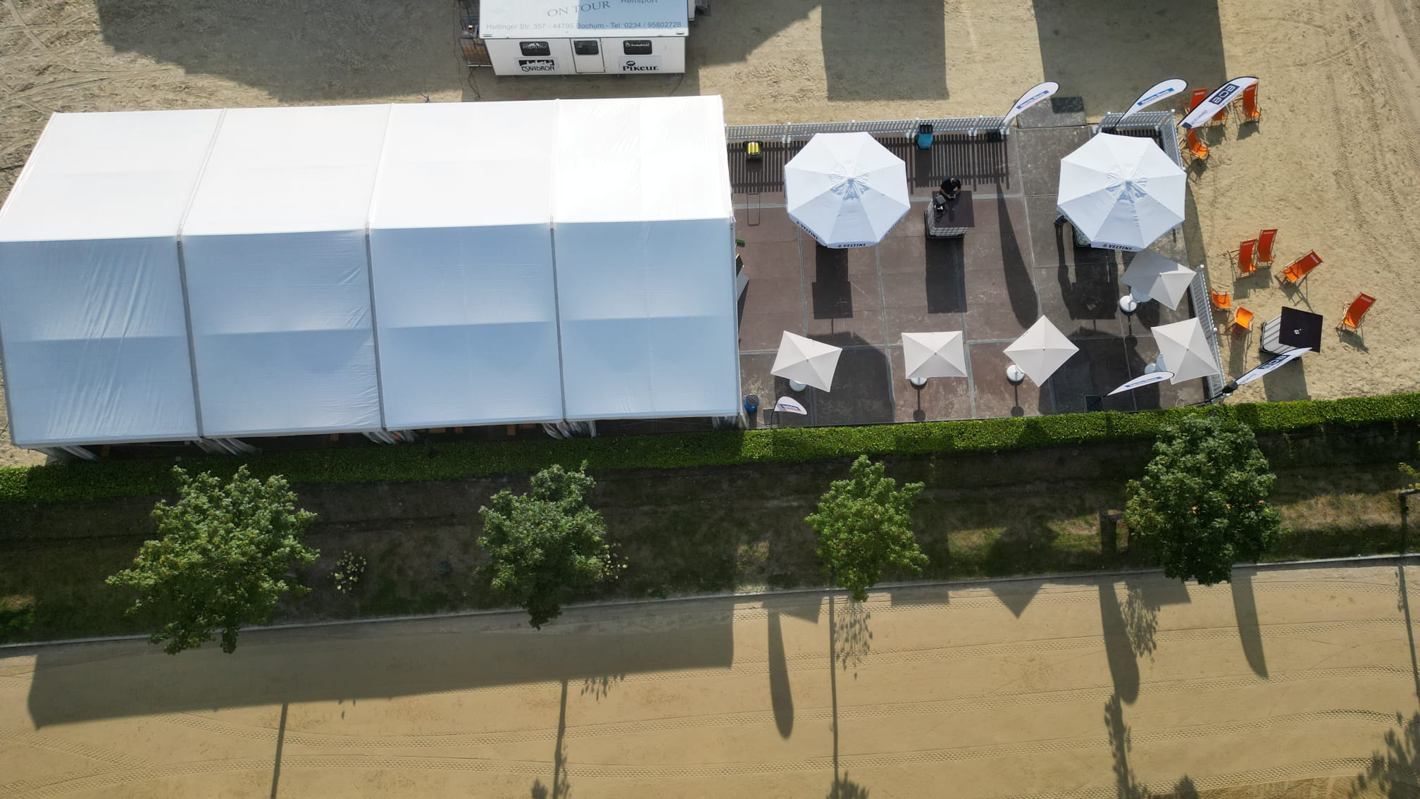 Weißes Festzelt und Terrasse mit Sonnenschirmen und orangenen Liegestühlen