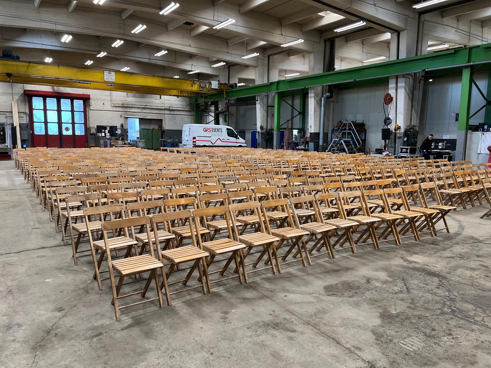 Viele leere Holzstühle stehen ordentlich in Reihen in einer großen Industriehalle