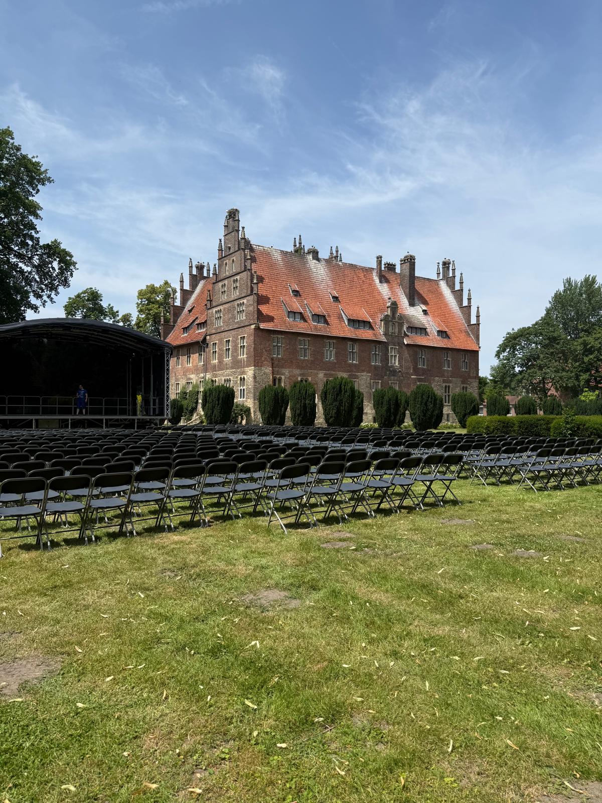 Ein altes Backsteinschloss mit rotem Dach und vielen leeren schwarzen Stühlen davor